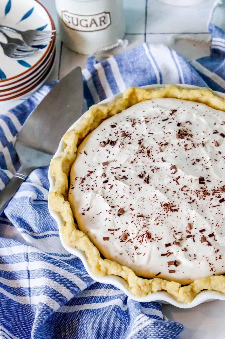 A homemade pie with a creamy filling and chocolate shavings on top, placed on a kitchen counter beside a sugar jar.