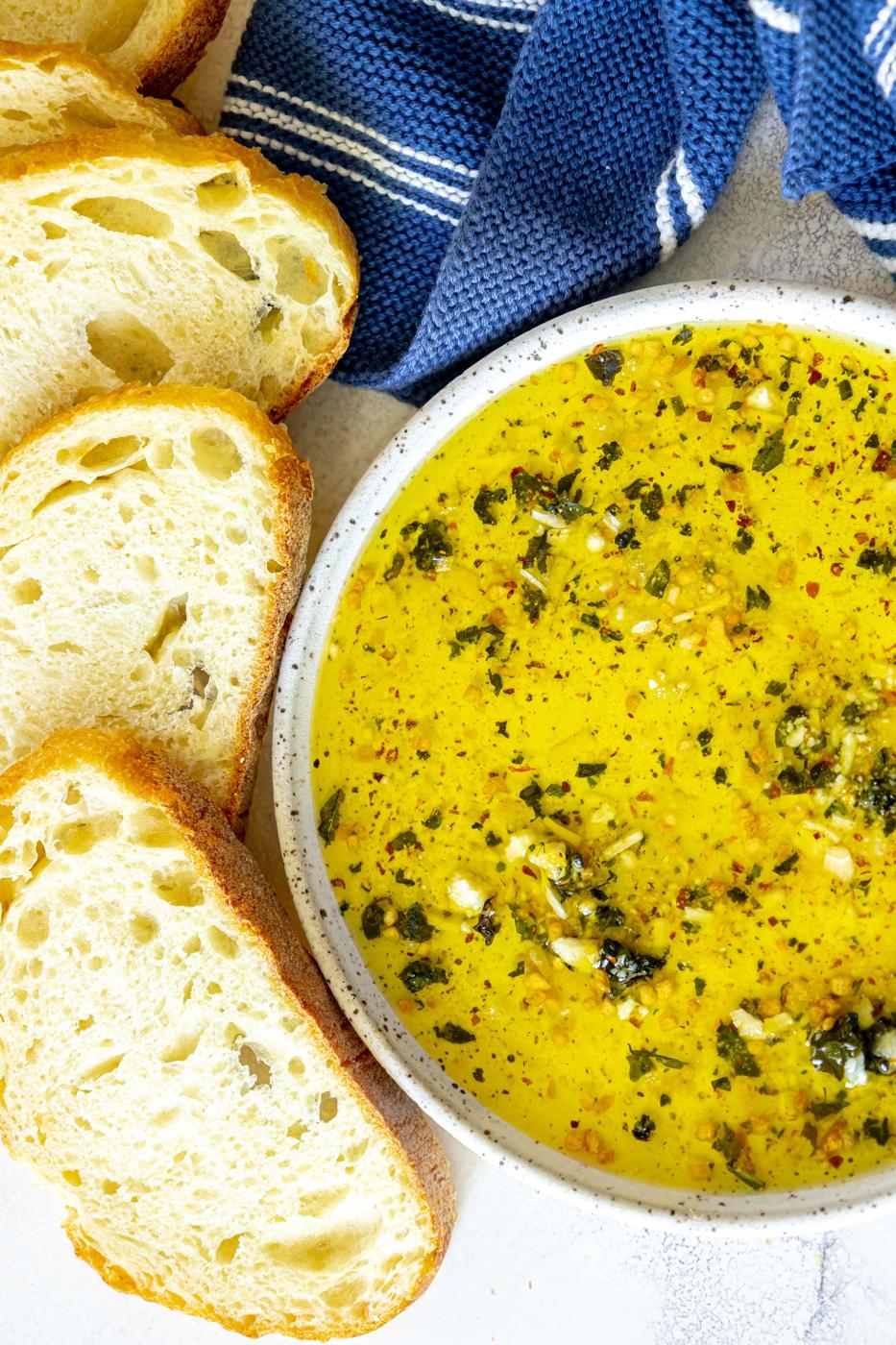 a slice of bread next to a bowl full of olive oil bread dip