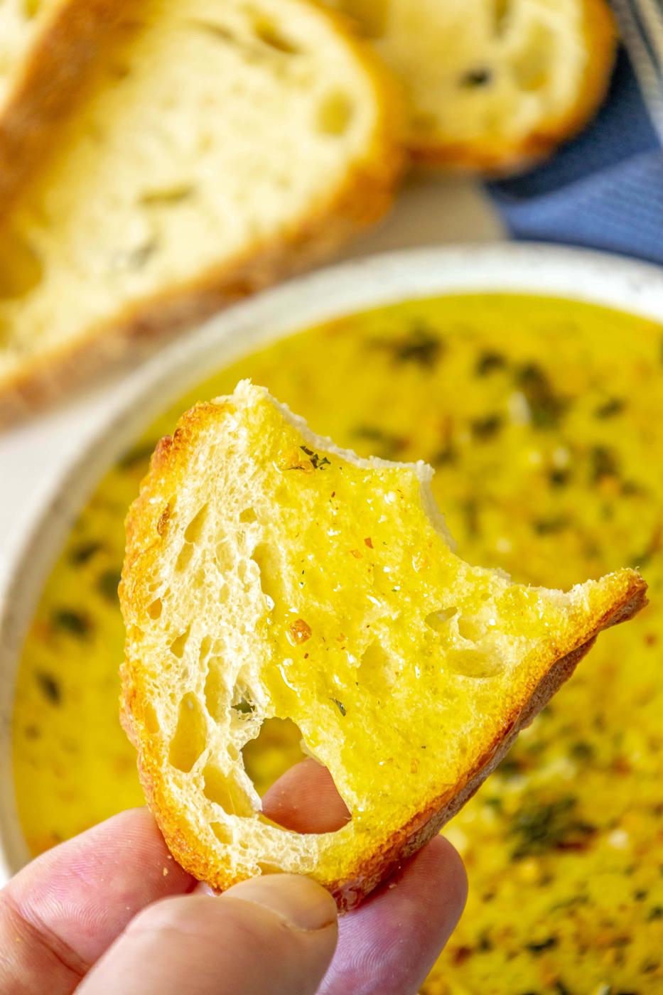 a slice of bread next to a bowl full of olive oil bread dip