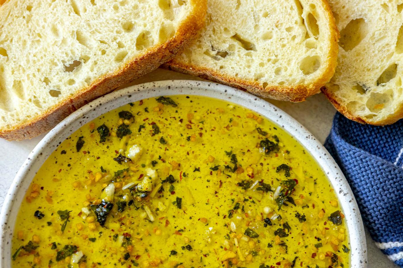 a slice of bread next to a bowl full of olive oil bread dip