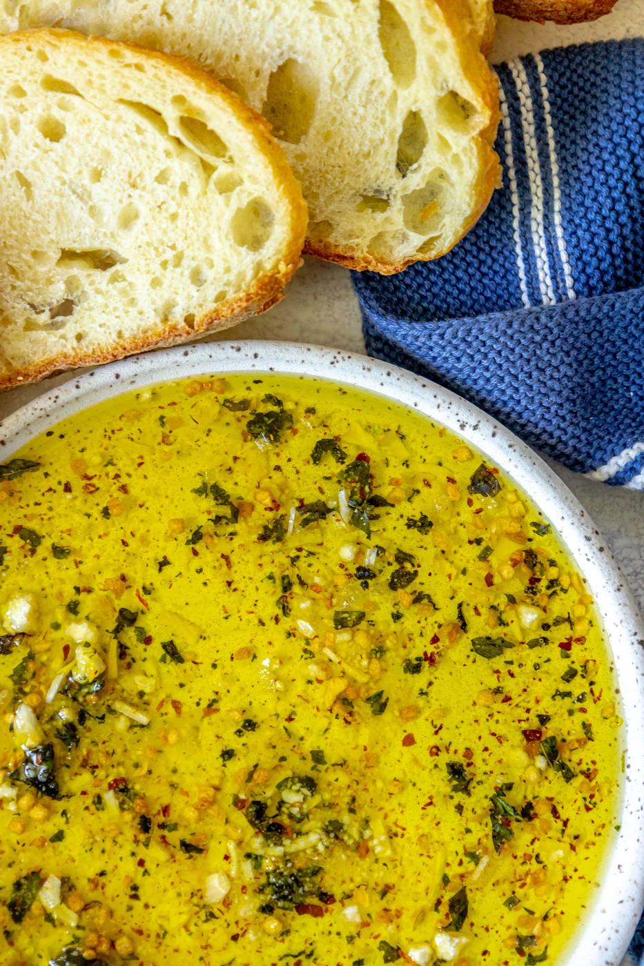 a slice of bread next to a bowl full of olive oil bread dip