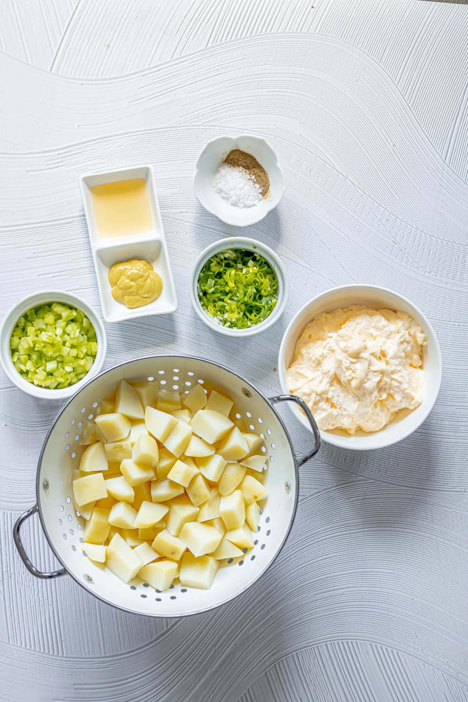 picture of boiled potatoes, mayo, onions, celery, mustard, cider, and seasonings on a table