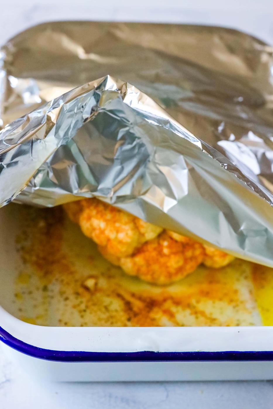 Foil wrapped chicken in a baking dish, keto roasted cauliflower.