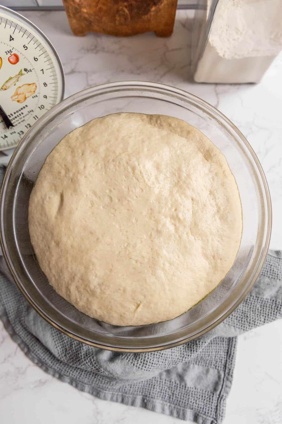 Dough in a glass bowl next to a measuring cup.