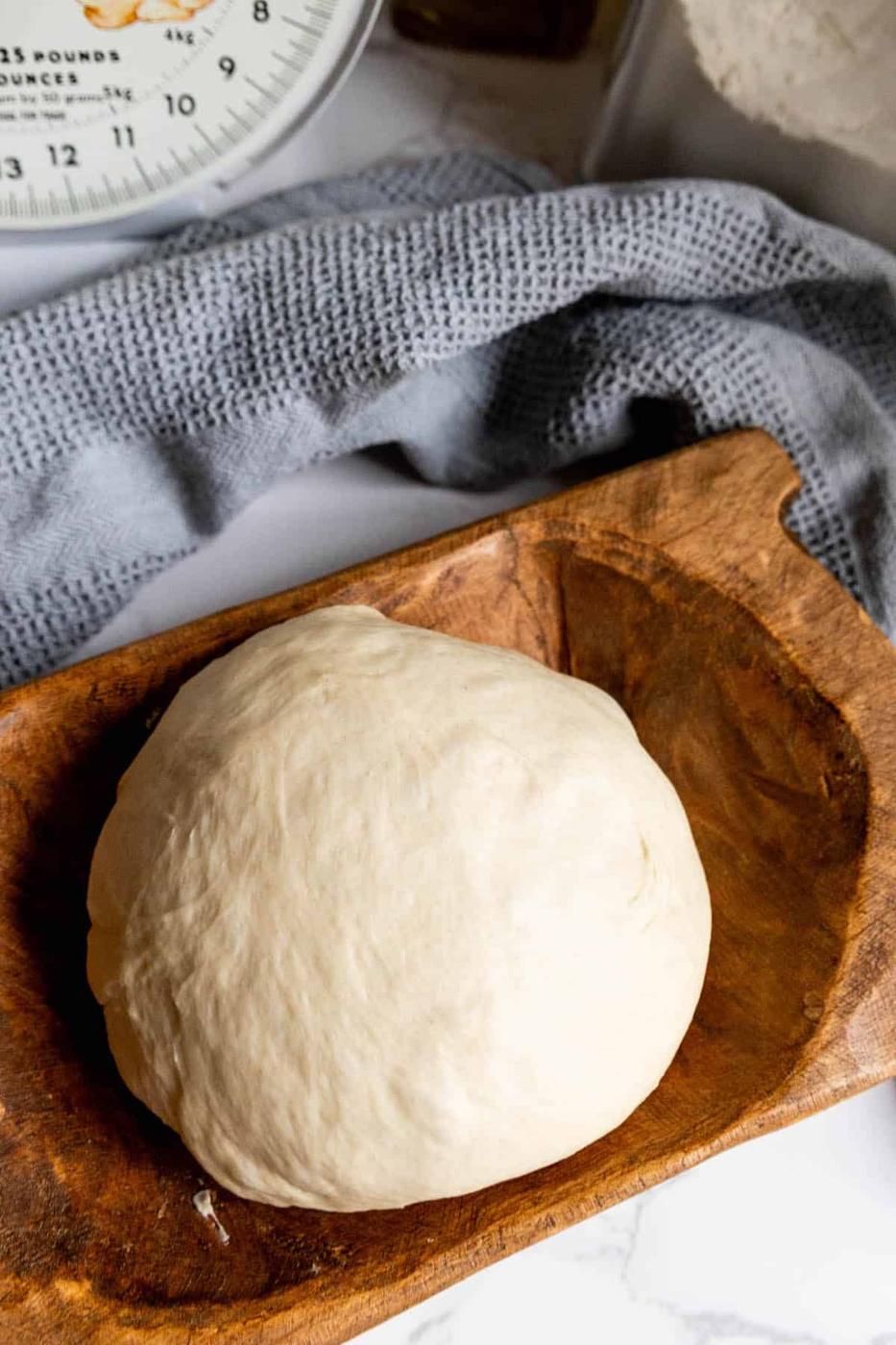 A dough ball on a wooden board next to a measuring scale.