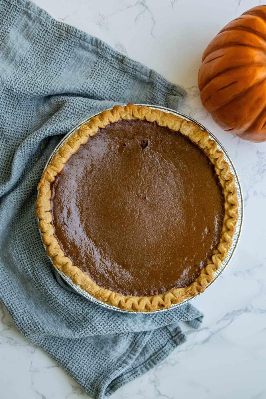 A pumpkin pie is sitting on a table next to a orange pumpkin.