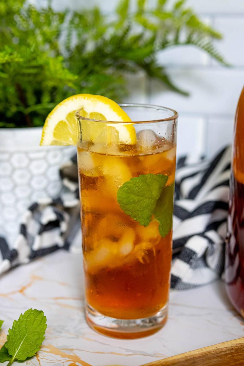 a tall glass with tea, ice, mint, and slices of lemon in it