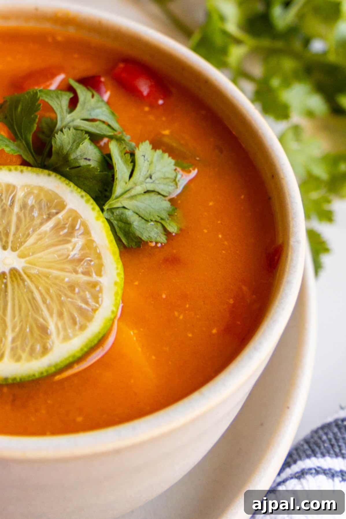 A vibrant bowl of Vegan Thai Curry Soup garnished with a fresh lime wedge and a red chili.