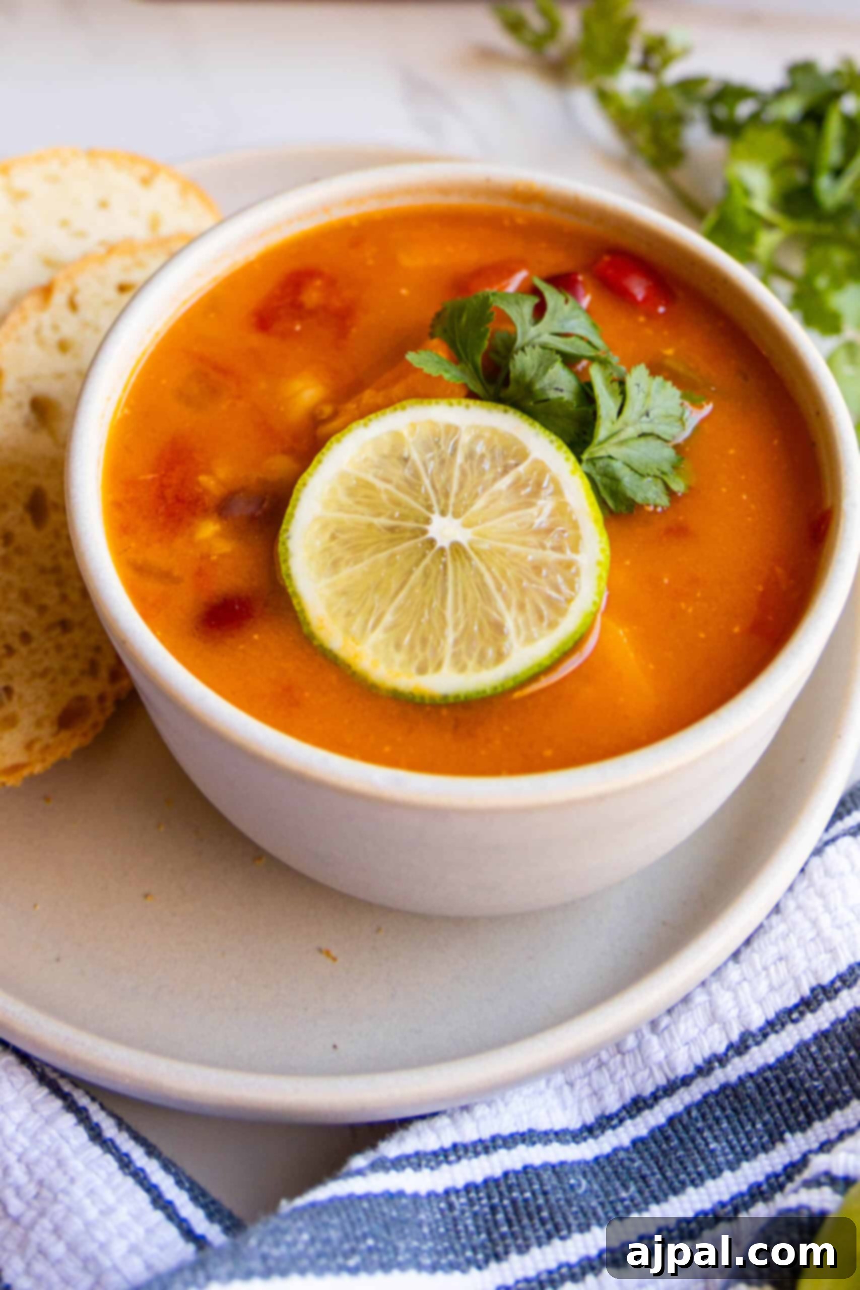 A cozy bowl of Vegan Thai Curry Soup with a slice of bread on the side, inviting you to enjoy.