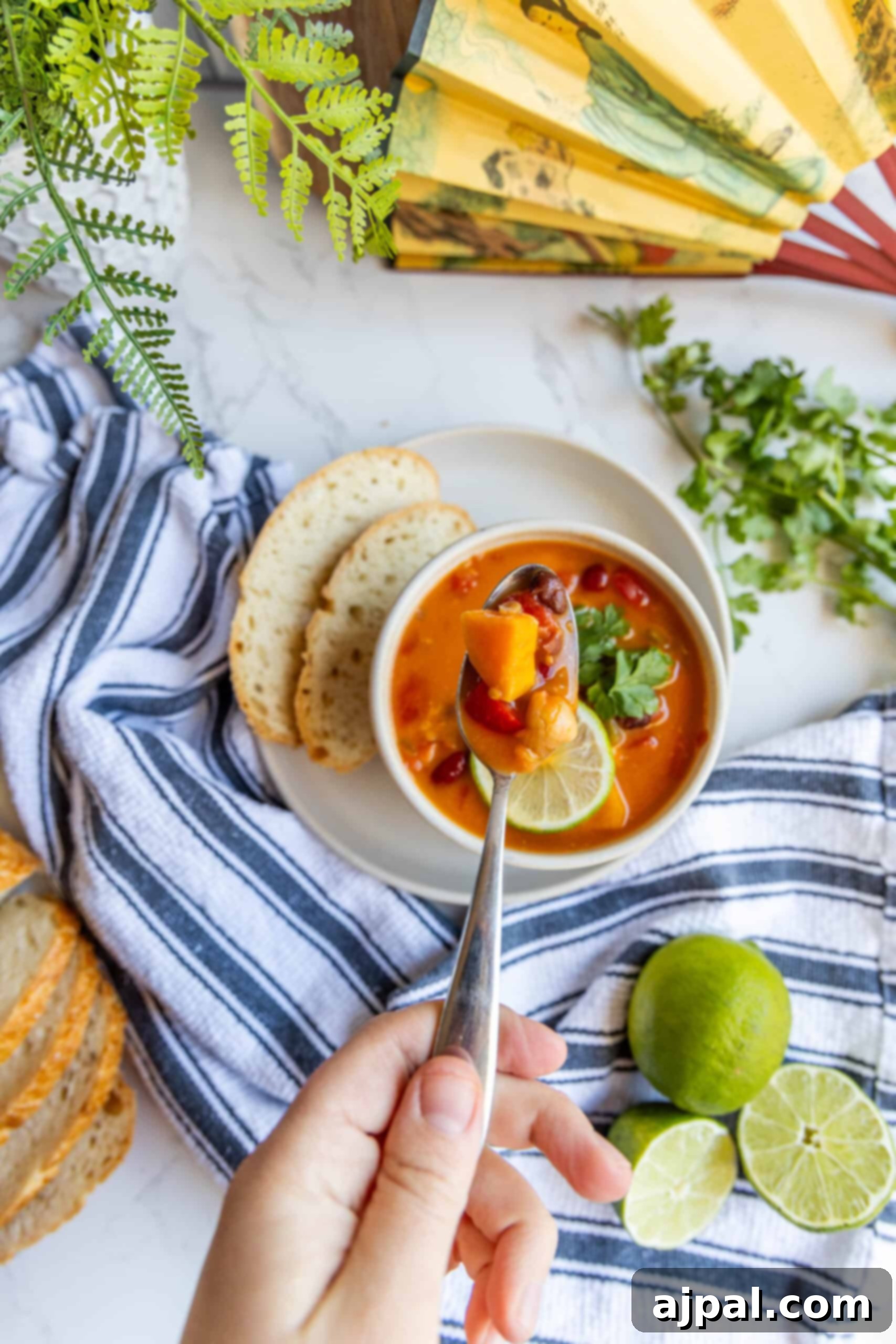 A person holding a bowl of Vegan Thai Curry Soup with a slice of bread, ready to enjoy.