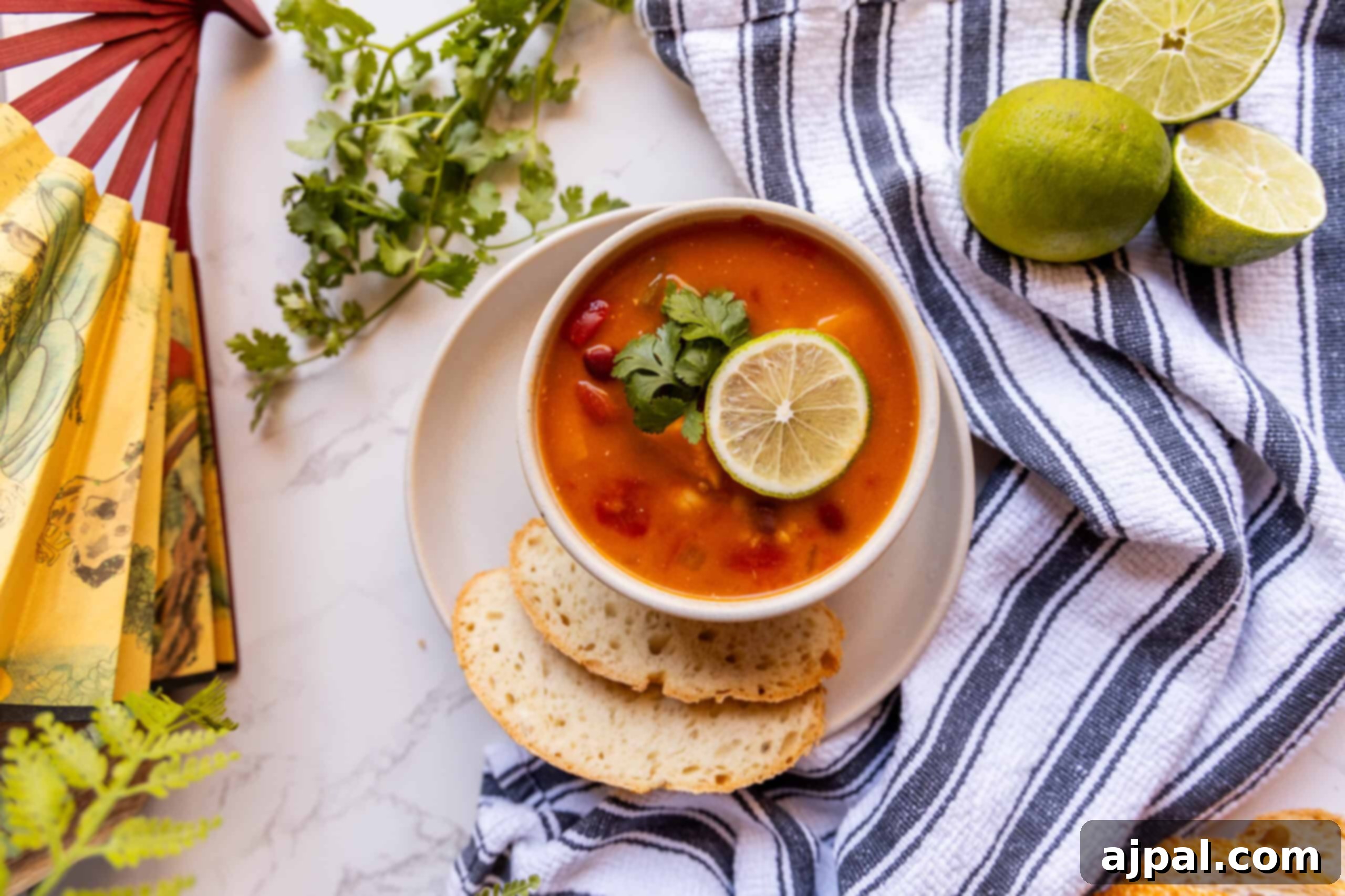 A delicious bowl of Vegan Thai Curry Soup, garnished with lime and chili, sitting on a rustic wooden table.