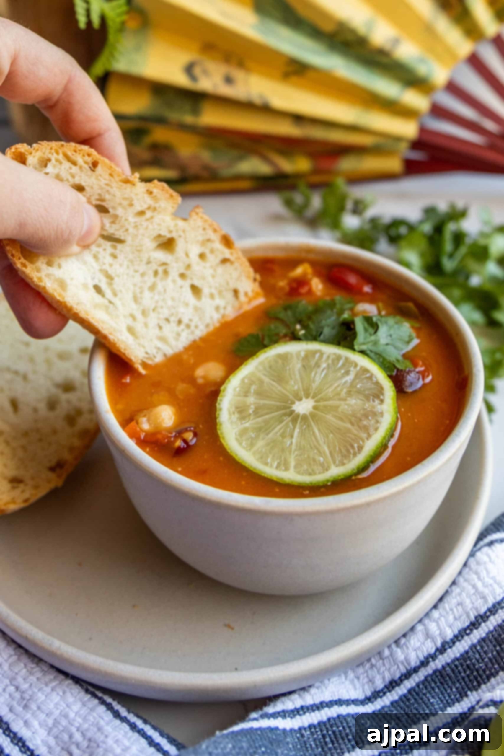 A person dipping a piece of crusty bread into a steaming bowl of Vegan Thai Curry Soup, showcasing its inviting texture.