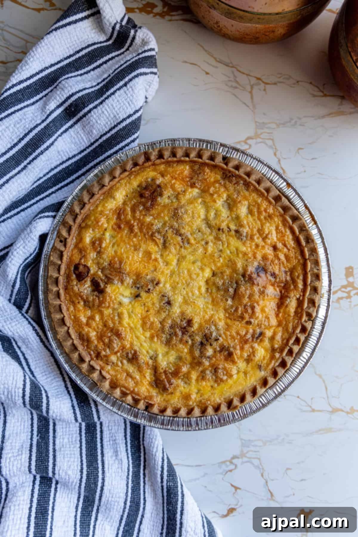 A golden brown bacon quiche sitting on a wooden table next to a patterned towel.