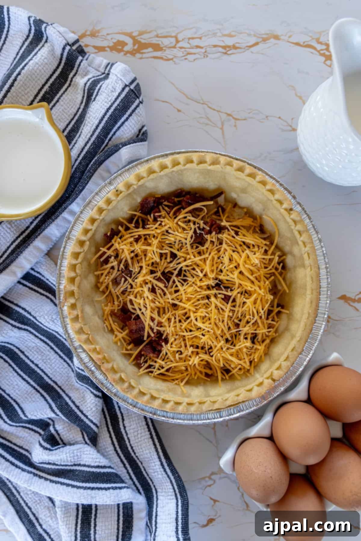 A quiche with bacon and cheese in a pie pan, freshly assembled before baking.