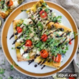 A plate of flatbread pizza with tomatoes and greens on it, highlighting the vibrant final product.