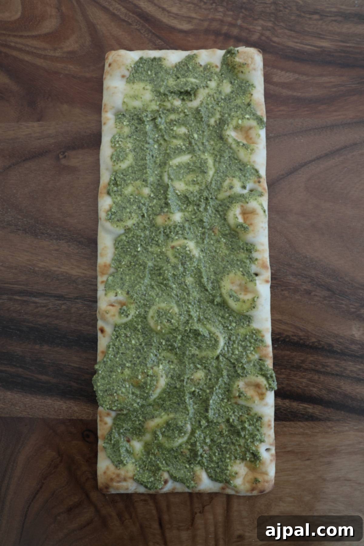 Artisan Pesto Chicken Flatbread 6 A rustic flatbread pizza base evenly coated with vibrant green pesto, waiting for toppings on a wooden surface.