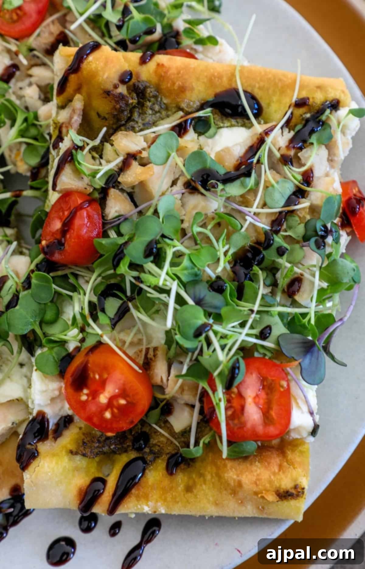 Artisan Pesto Chicken Flatbread 9 A freshly baked flatbread pizza, adorned with vibrant red tomatoes and crisp green arugula, beautifully arranged on a plate.