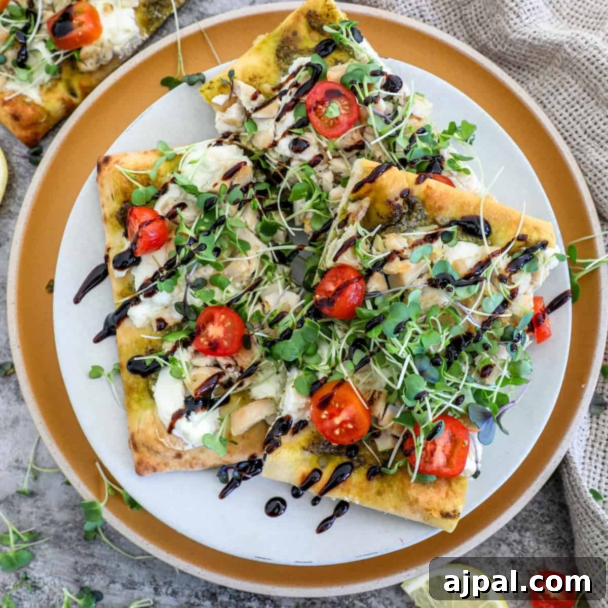 Artisan Pesto Chicken Flatbread 10 A vibrant flatbread pizza, featuring juicy red tomatoes and fresh green arugula, presented elegantly on a white plate.