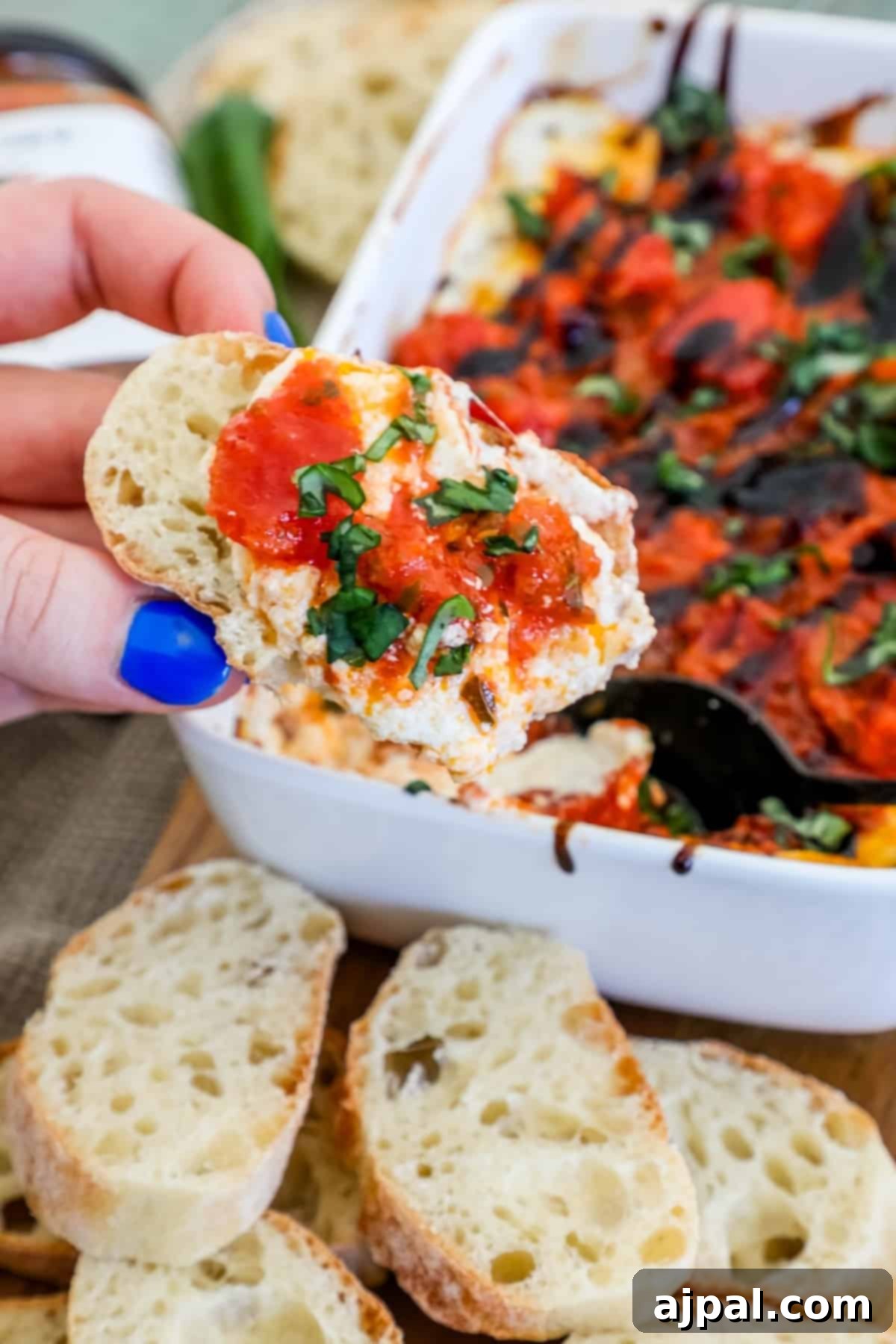 A hand reaches into a rustic dish, dipping a piece of crusty bread into the rich and vibrant bruschetta dip, invitingly presented.
