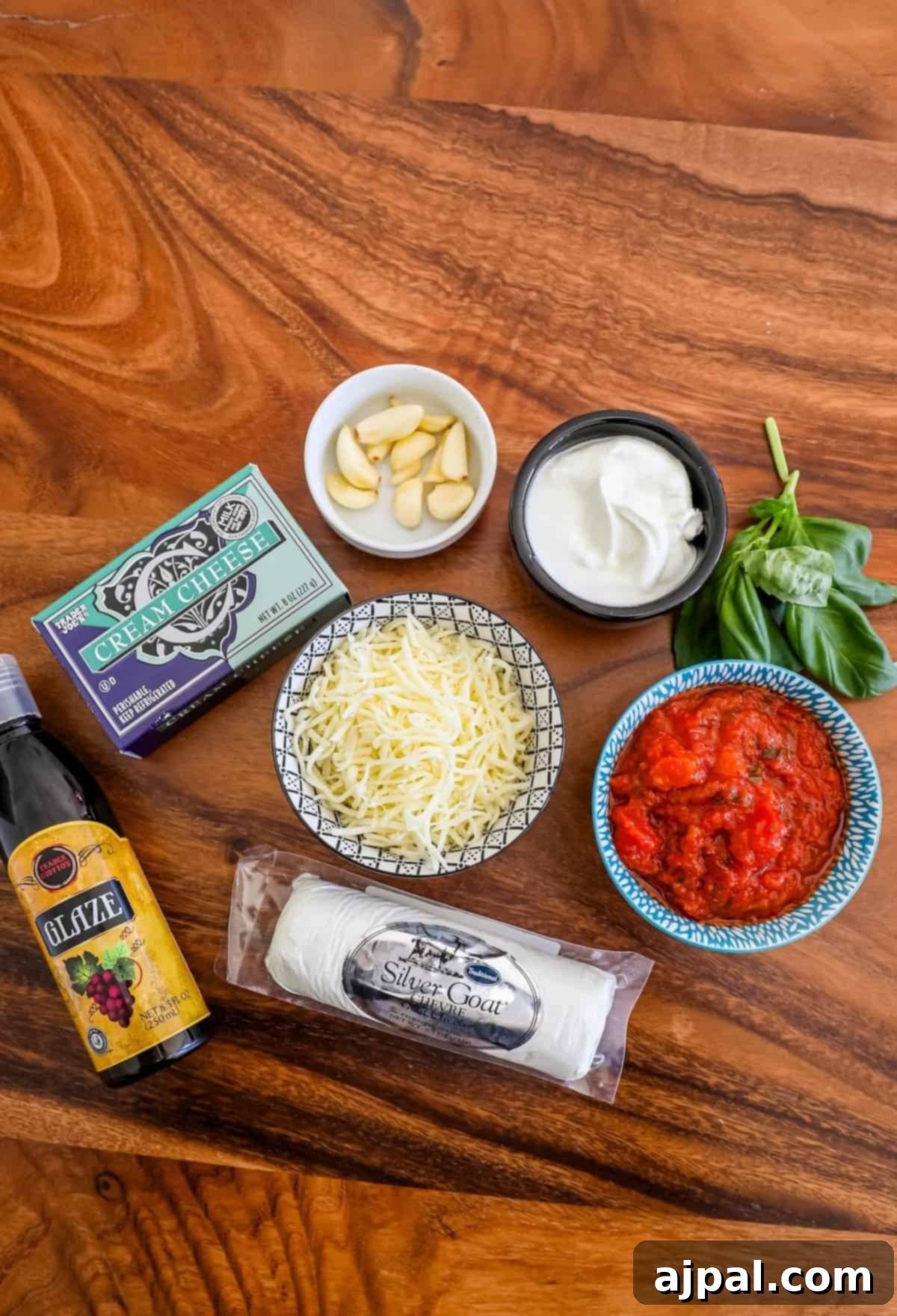 On a wooden table, fresh ingredients for a delightful appetizer are neatly arranged, featuring a creamy baked goat cheese and vibrant bruschetta dip as the centerpiece.