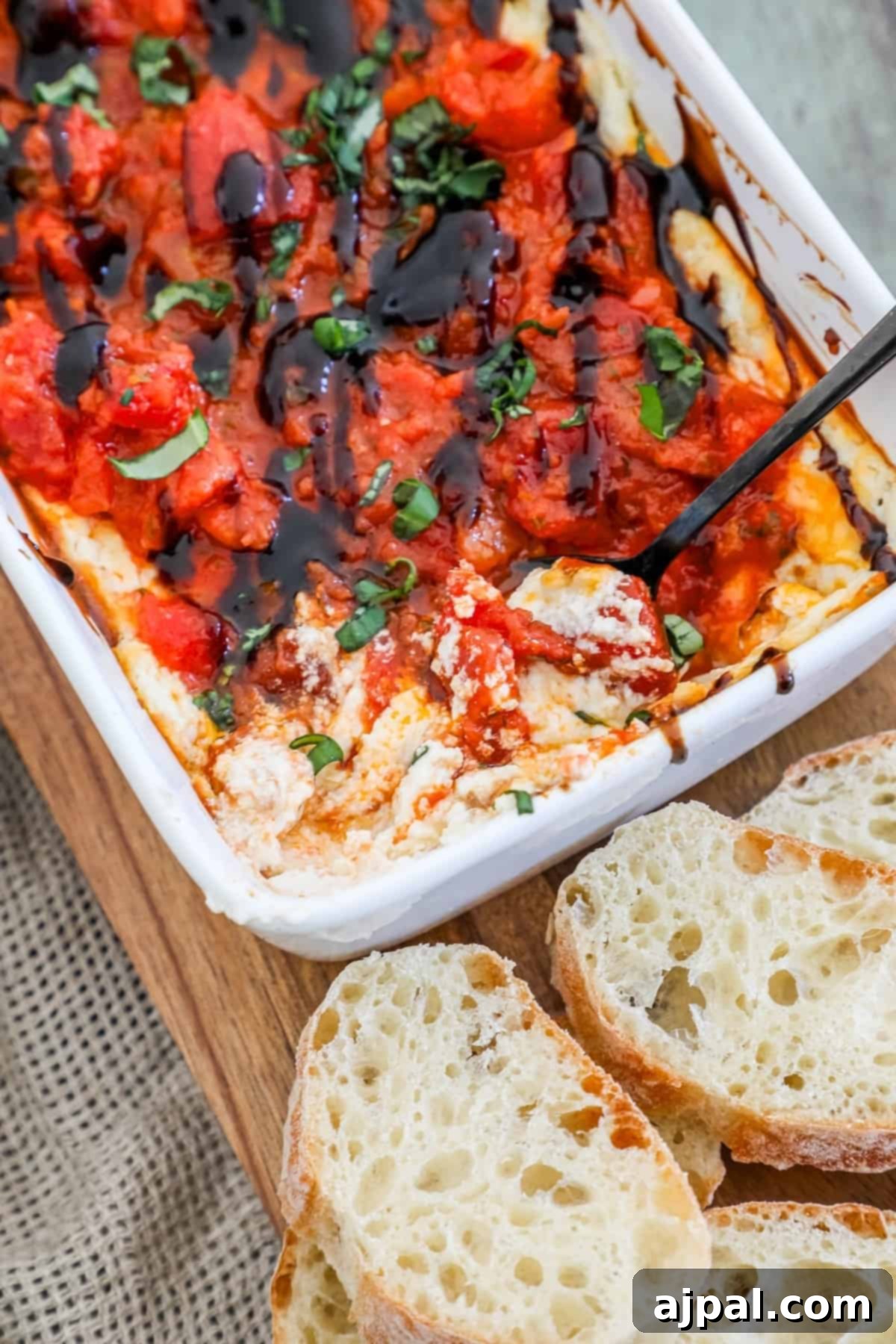 A vibrant dish of tomato dip, exquisitely presented with slices of toasted bread on a wooden cutting board, serving as the perfect complement to a rich baked goat cheese and bruschetta dip.