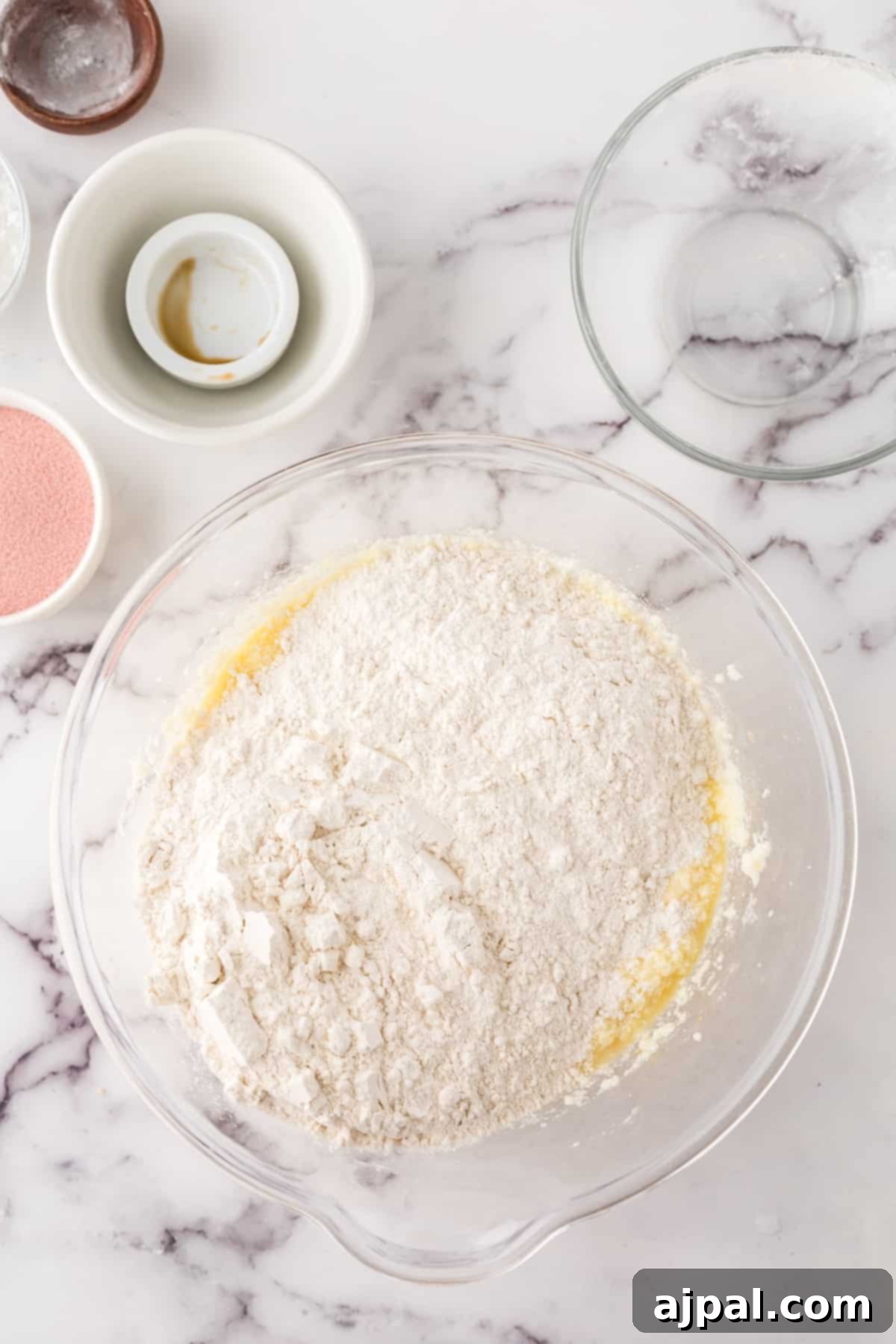 A close-up shot of a bowl brimming with all-purpose flour, surrounded by other essential baking ingredients like eggs and milk, all set on a cool marble surface, hinting at the start of a delightful baking session.