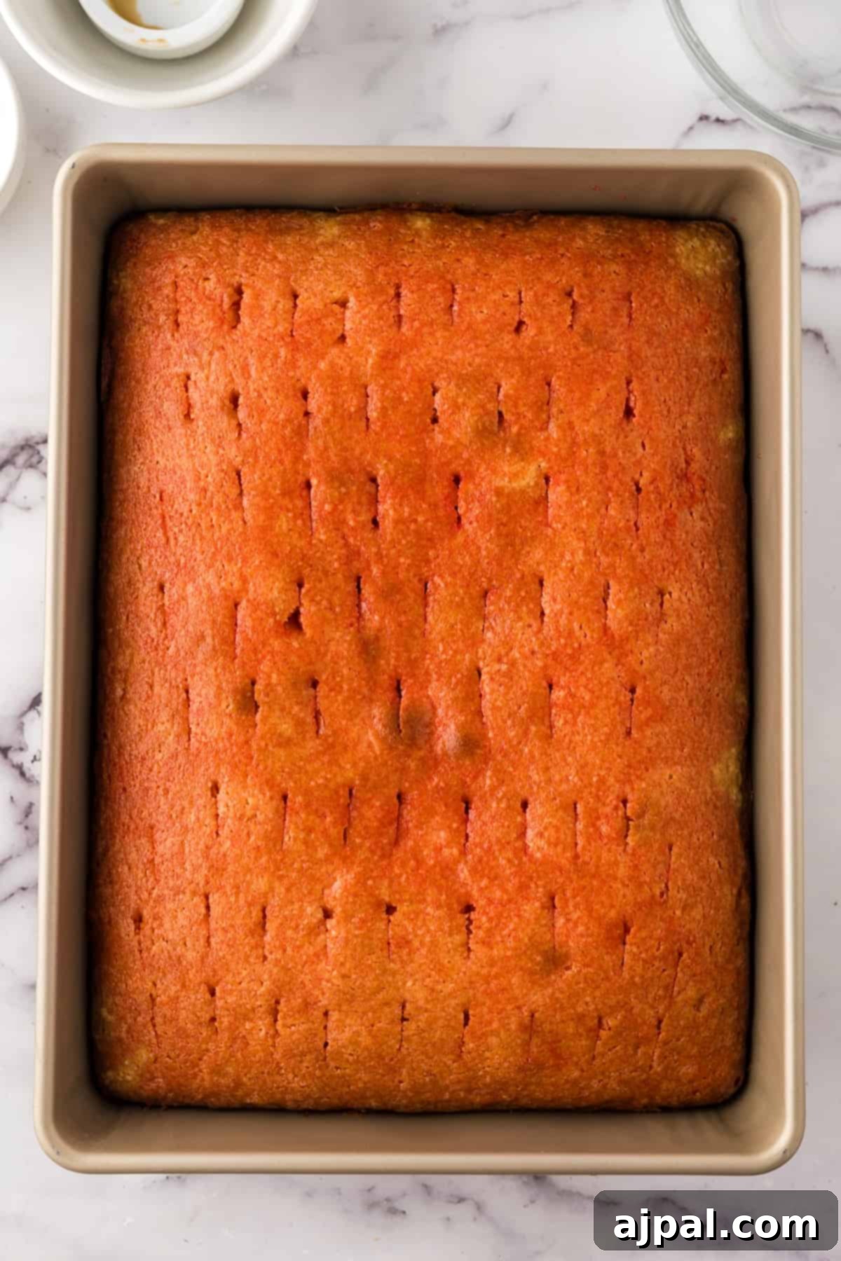 A perfectly baked, golden-brown sheet cake, freshly out of the oven and still in its baking pan, hints at its rich flavor. It's ready to be soaked with a delightful raspberry sauce and frosted.