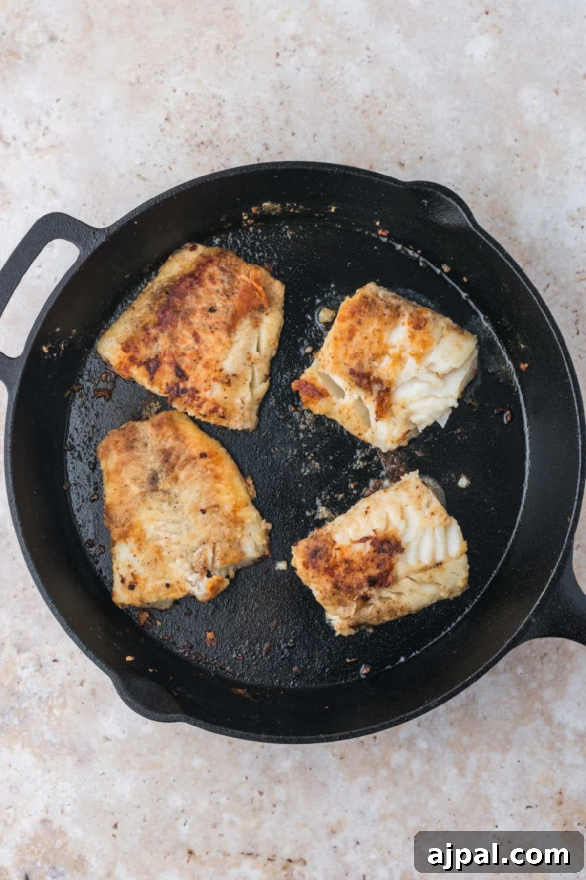 Golden Pan-Seared Cod 11 Another view of pan-fried cod fillets in a cast iron skillet, nearly finished cooking, displaying a beautiful golden-brown color.