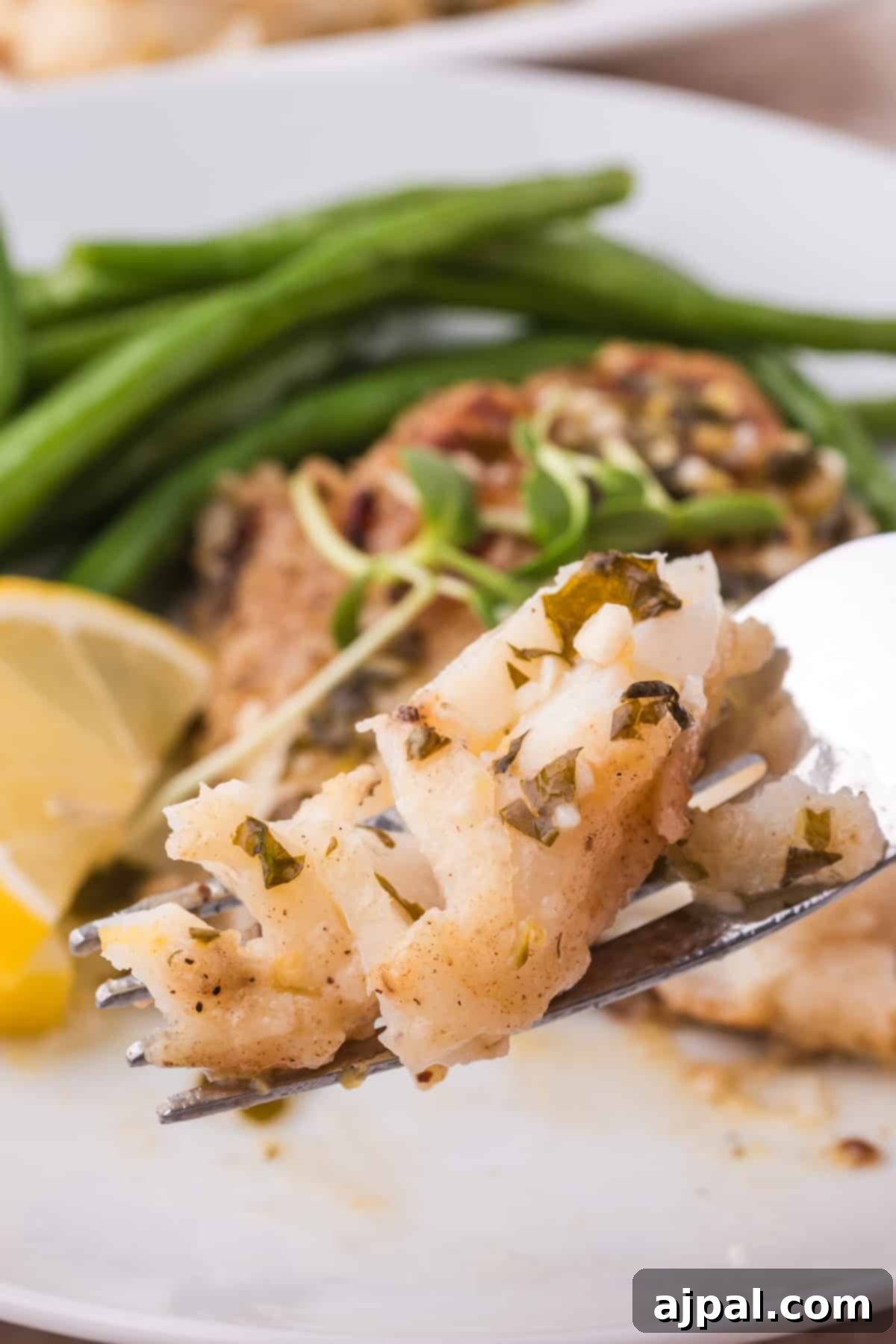 Golden Pan-Seared Cod 4 A fork lifts a delicate piece of pan-fried cod along with some green beans from a serving plate, highlighting the tender flakes of the fish and the fresh side dish.