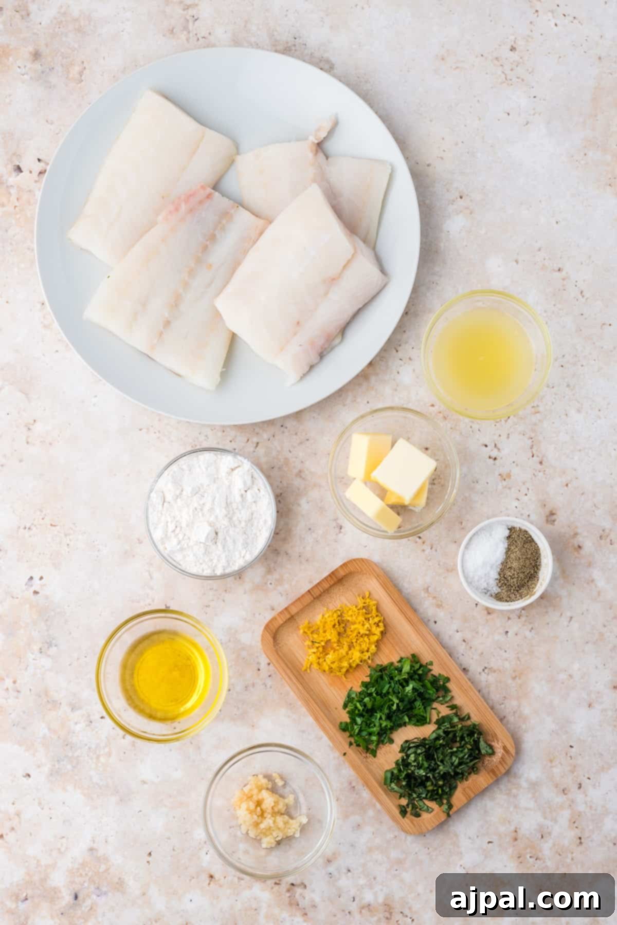 Golden Pan-Seared Cod 5 A collection of fresh ingredients for pan-fried cod, including cod fillets, lemon, herbs, garlic, and butter, neatly arranged on a white plate, ready for preparation.