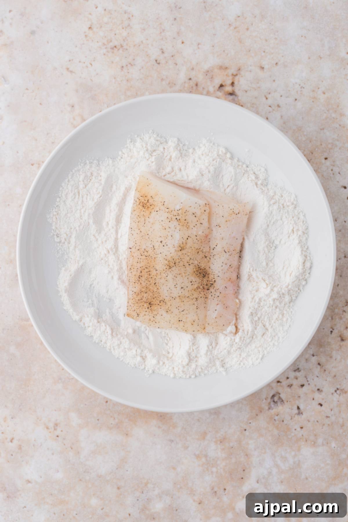 Golden Pan-Seared Cod 9 A single cod fillet with a perfect golden-brown flour coating on a white plate, showcasing its crispy texture achieved through pan-frying.