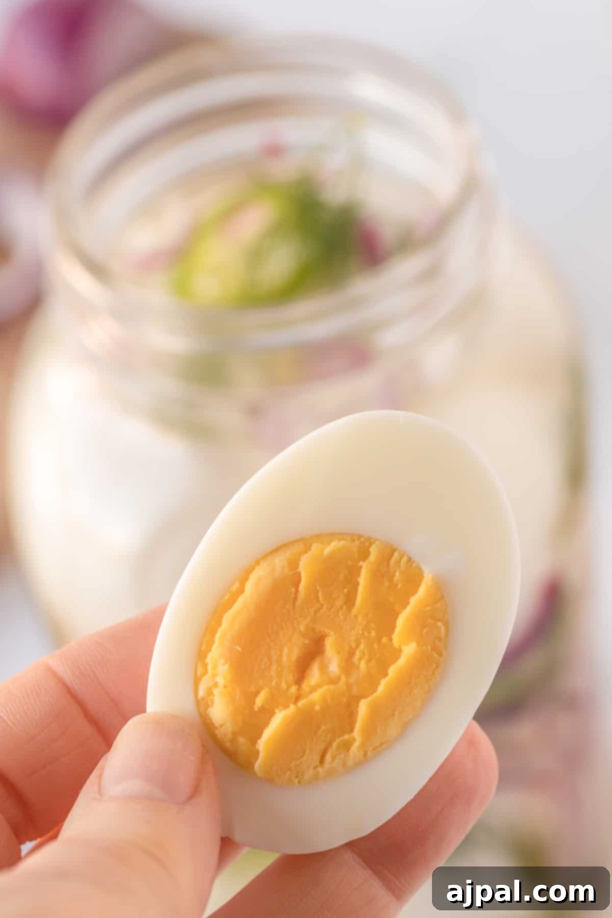 A person holding a hard boiled egg in front of a jar of pickled eggs.