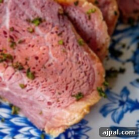 A glistening piece of roasted corned beef, ready to be sliced, on a blue and white plate.