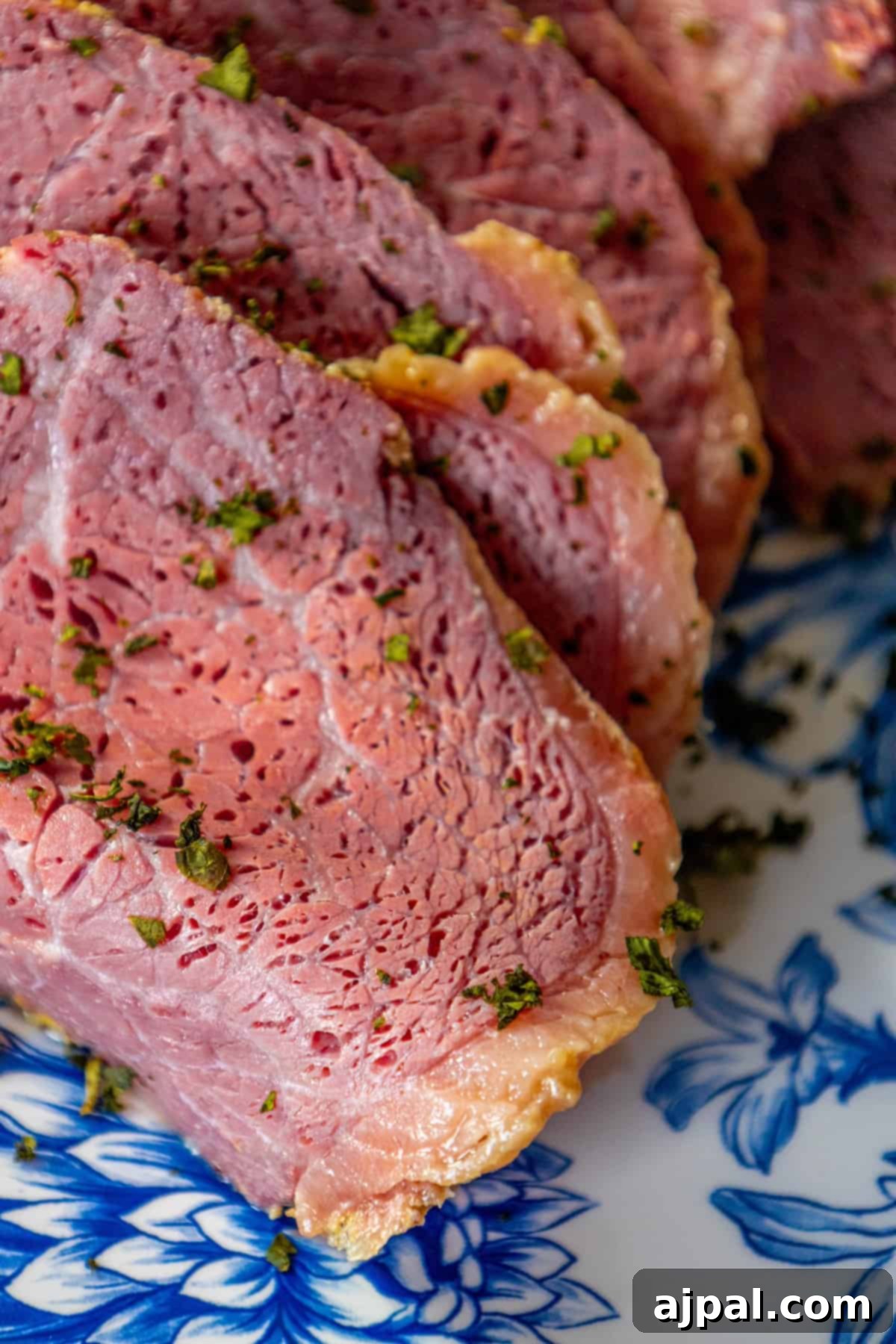 Perfectly Roasted Corned Beef 5 A close-up view of beautifully sliced, tender corned beef on a blue plate, highlighting its perfect glaze and inviting texture.