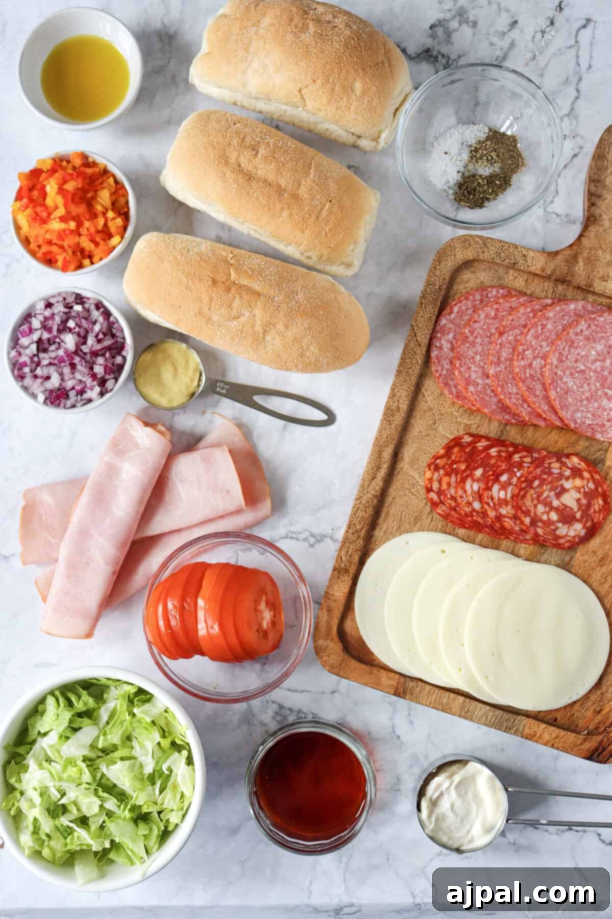 An array of fresh, high-quality ingredients for Italian sandwiches spread out on a wooden chopping board.