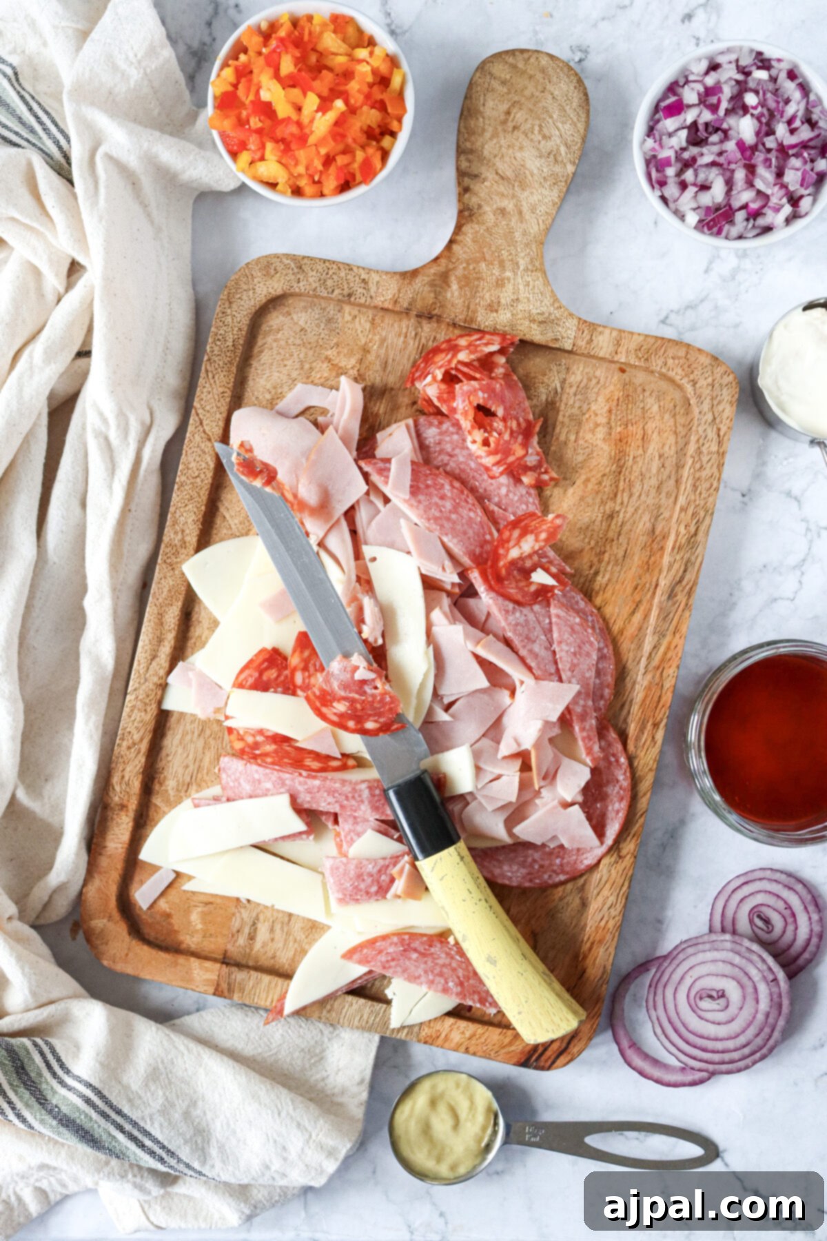 A cutting board featuring various Italian deli meats, red onions, and other fresh produce, perfectly laid out for sandwich preparation.