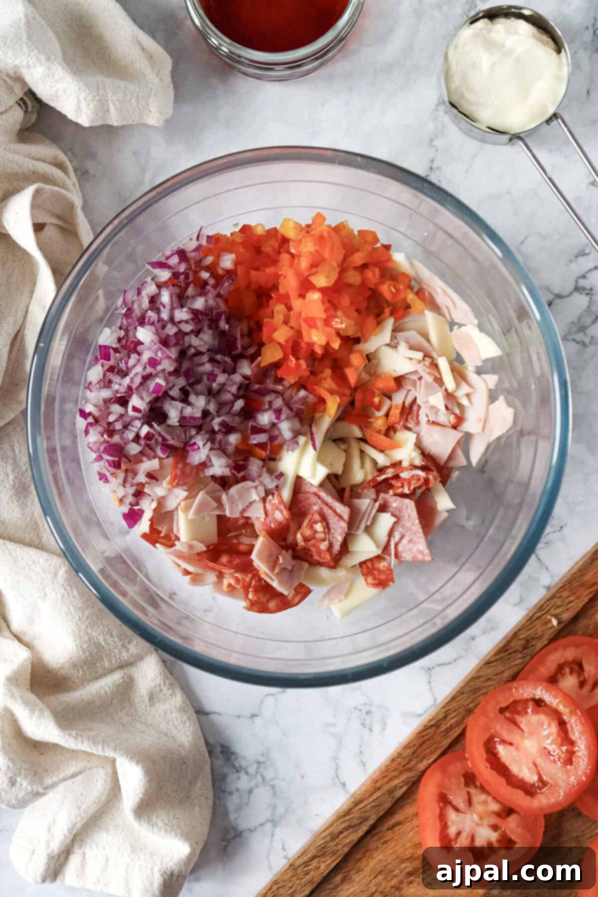 A bowl filled with freshly chopped tomatoes, onions, and ham, ready for mixing into a sandwich filling.