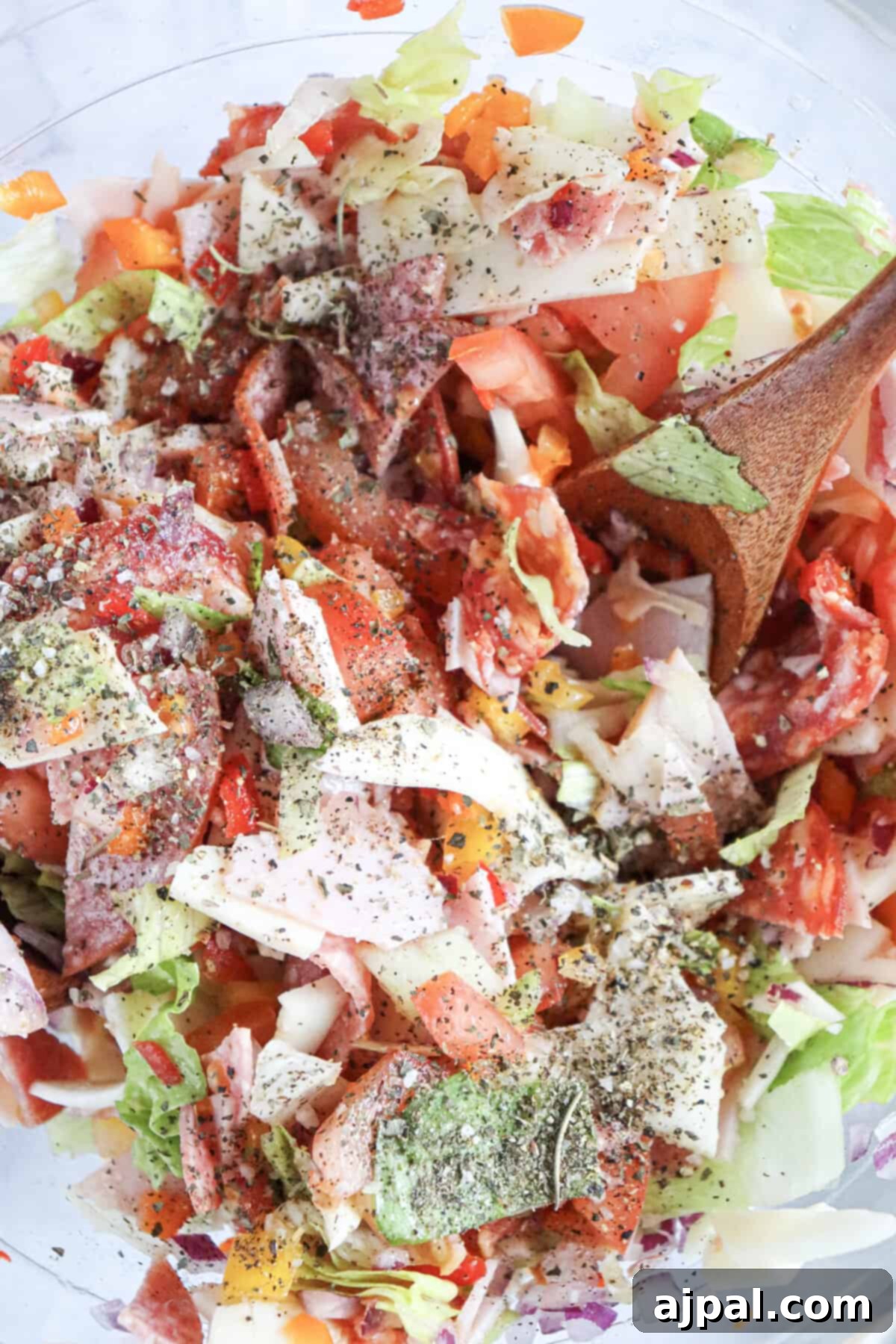 A bowl of vibrant chopped Italian salad, featuring a colorful mix of meats and fresh vegetables.
