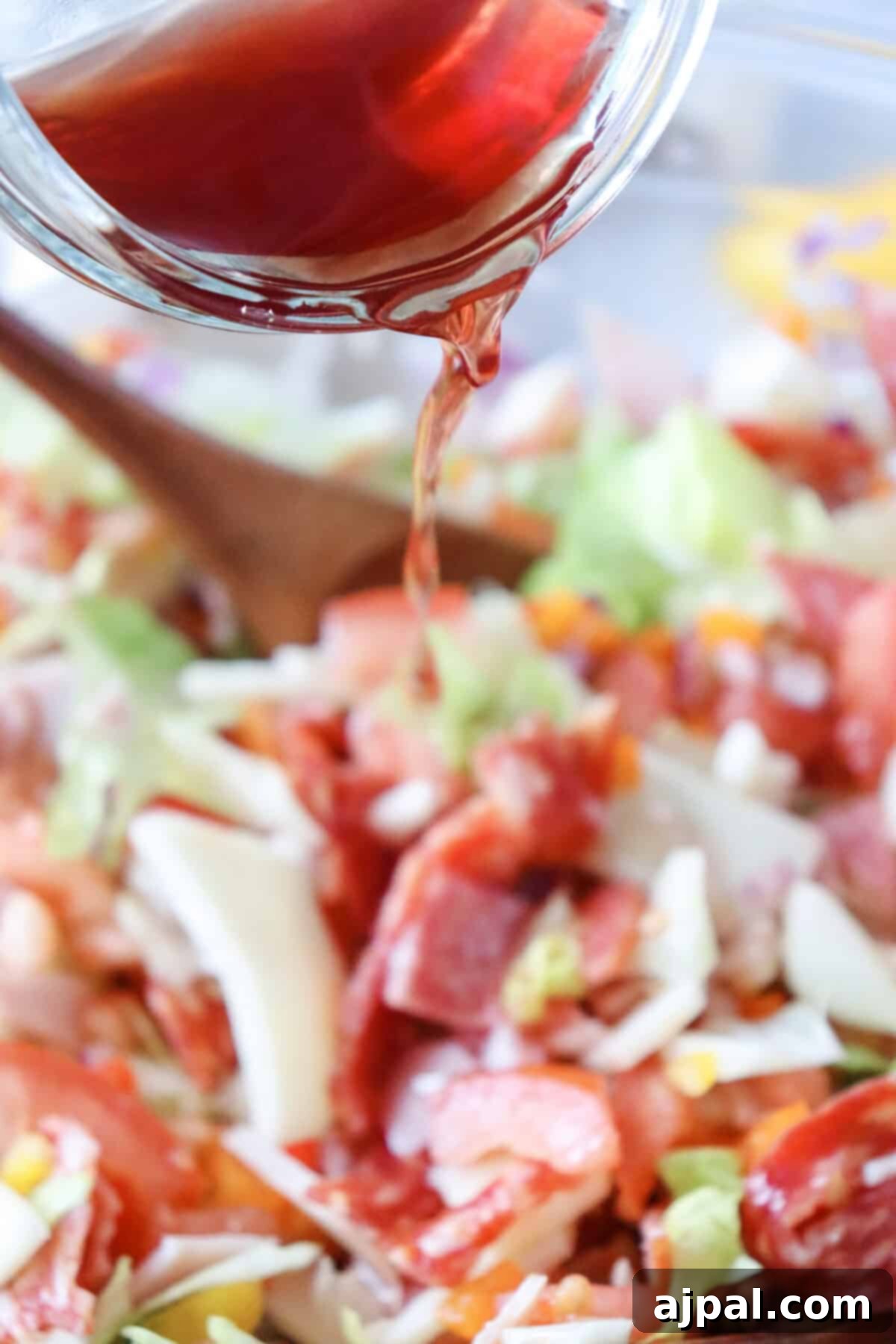 A spoon drizzles a zesty Italian dressing over a fresh, vibrant chopped salad in a bowl.