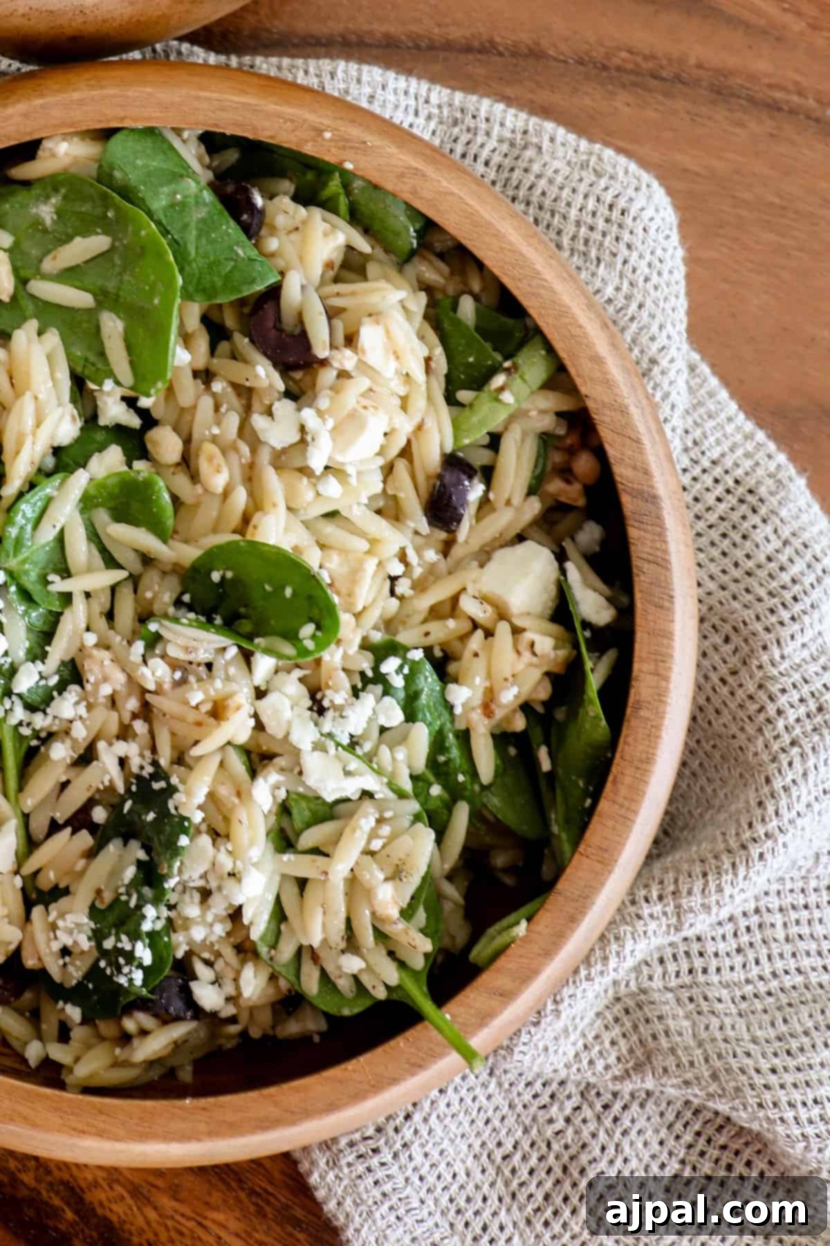Greek Spinach Feta Orzo Salad 2 A bowl of spinach and orzo salad topped with Feta cheese on a wooden table.