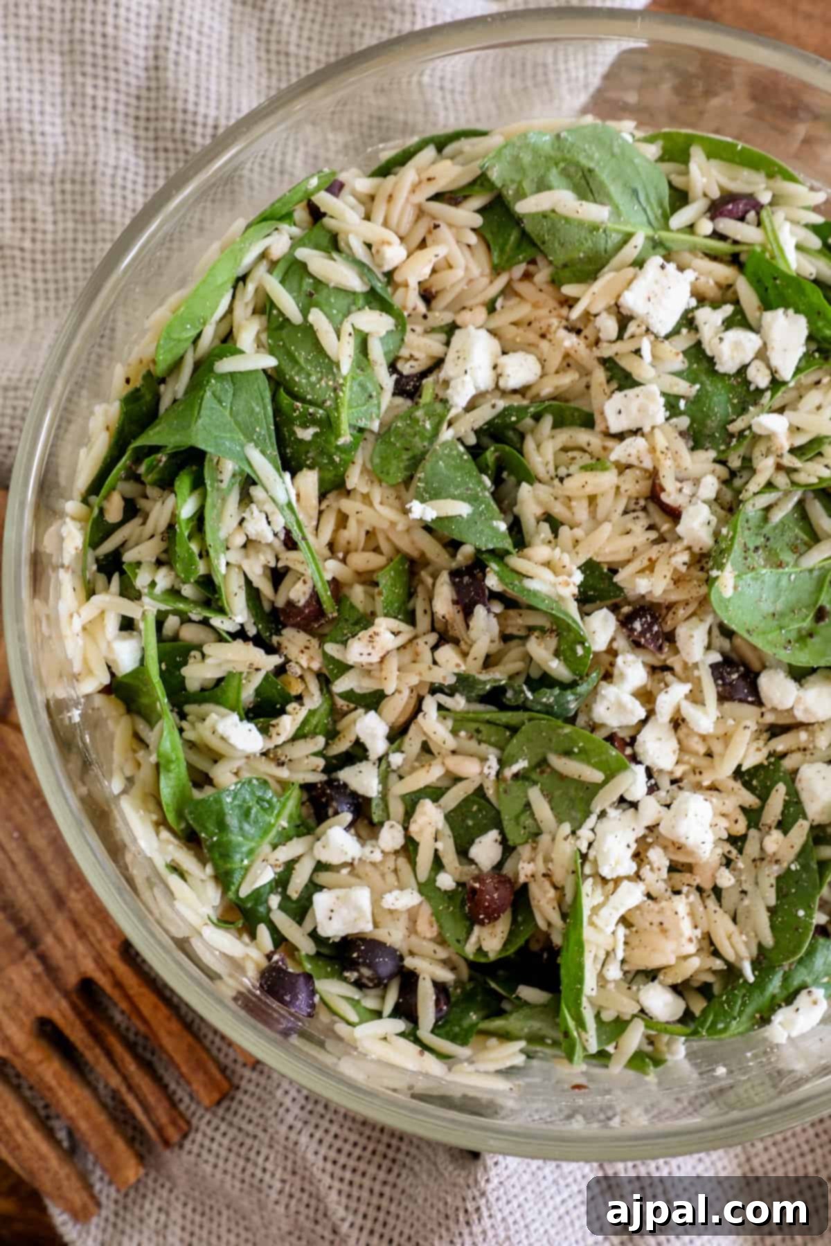 Greek Spinach Feta Orzo Salad 3 A bowl of spinach and feta salad with a wooden spoon next to it.