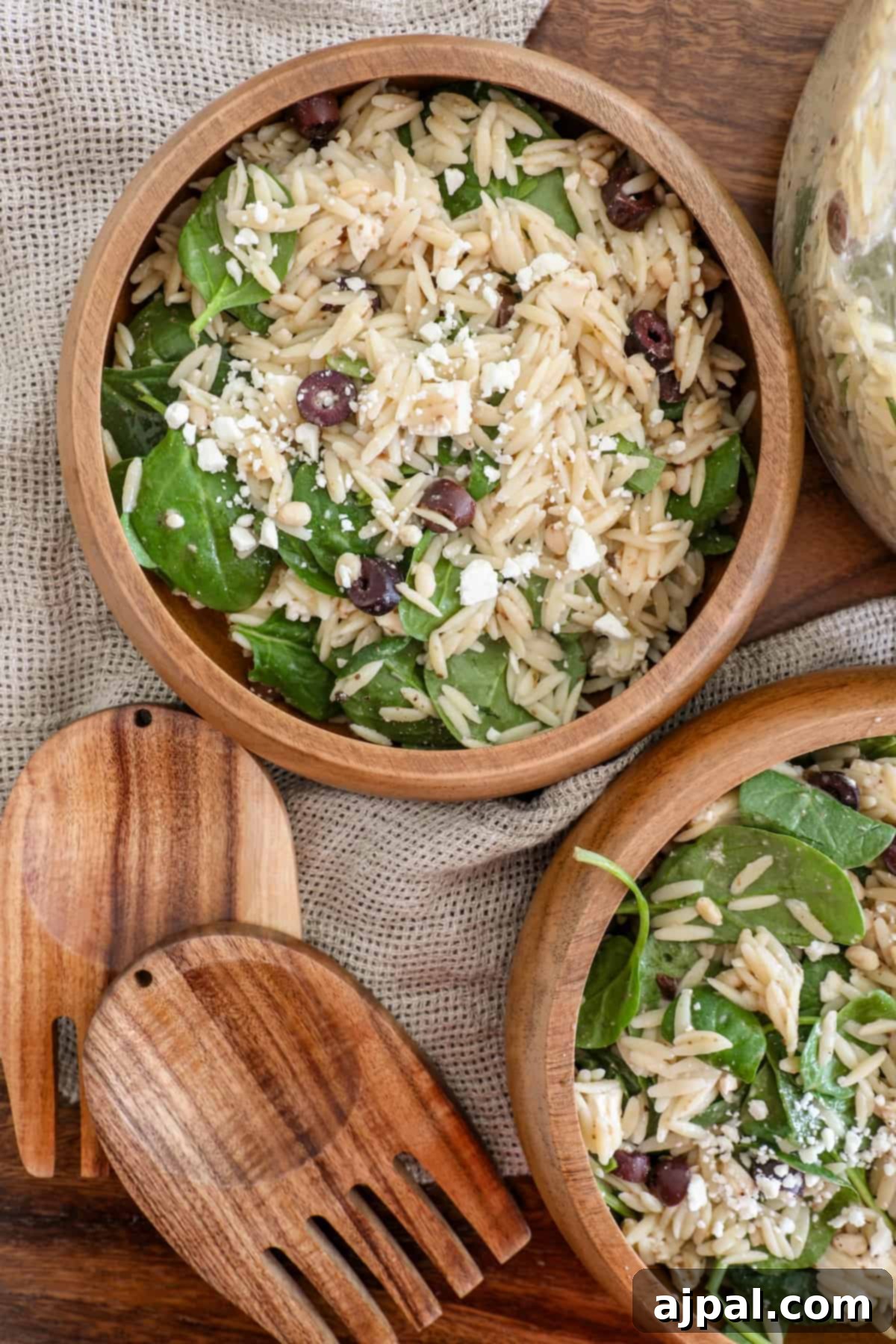Two aesthetically pleasing wooden bowls filled with a colorful mix of spinach and orzo, one generously topped with crumbled feta cheese.