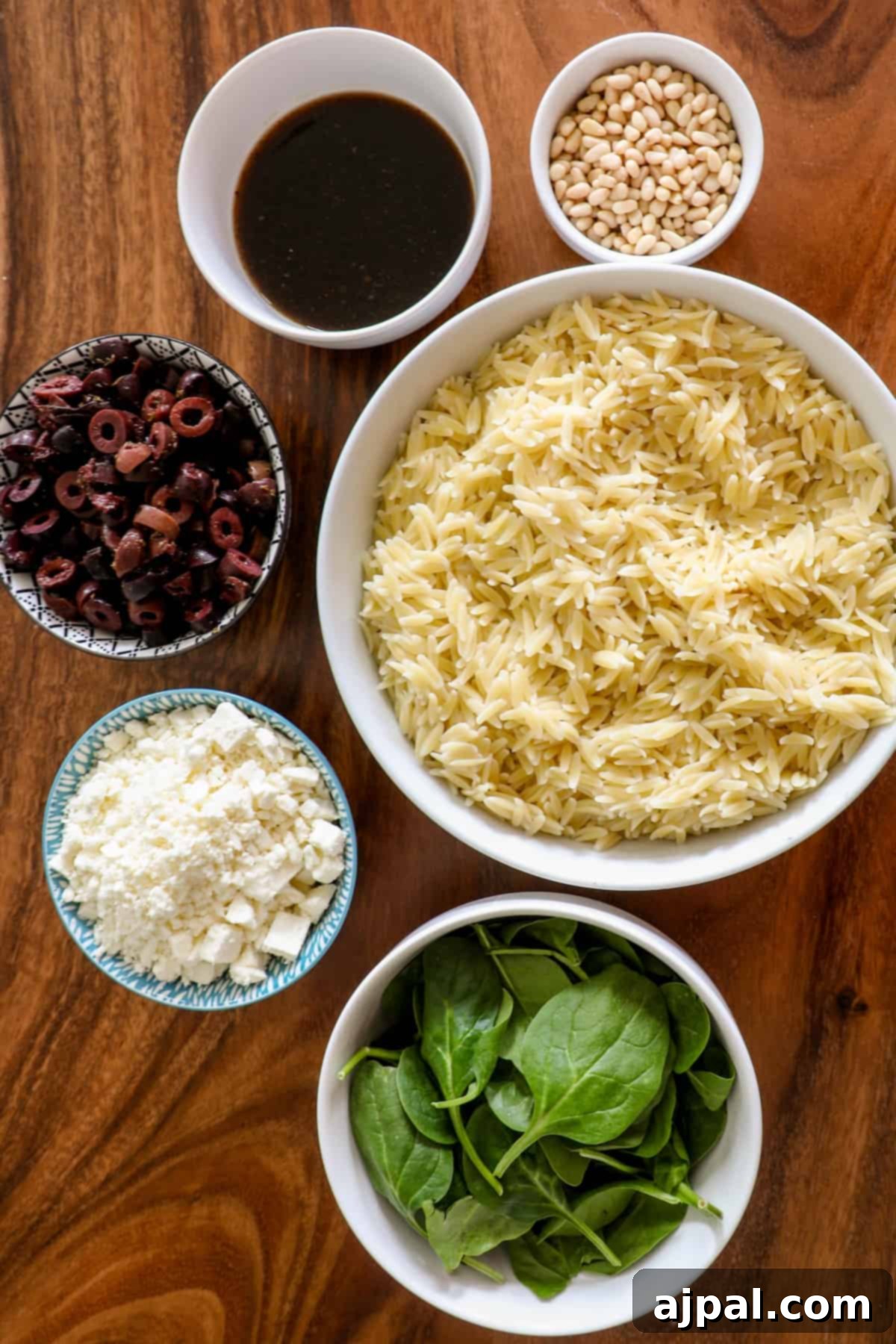 Greek Spinach Feta Orzo Salad 5 A bowl of orzo, spinach, and feta cheese on a wooden table.