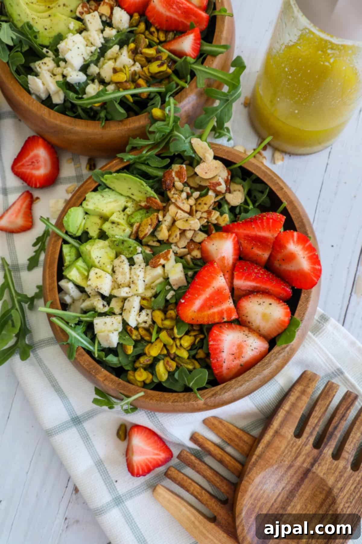 Two wooden bowls showcasing a vibrant Strawberry Crunch Salad, featuring fresh strawberries, crisp arugula, and creamy avocado, ready to be enjoyed.