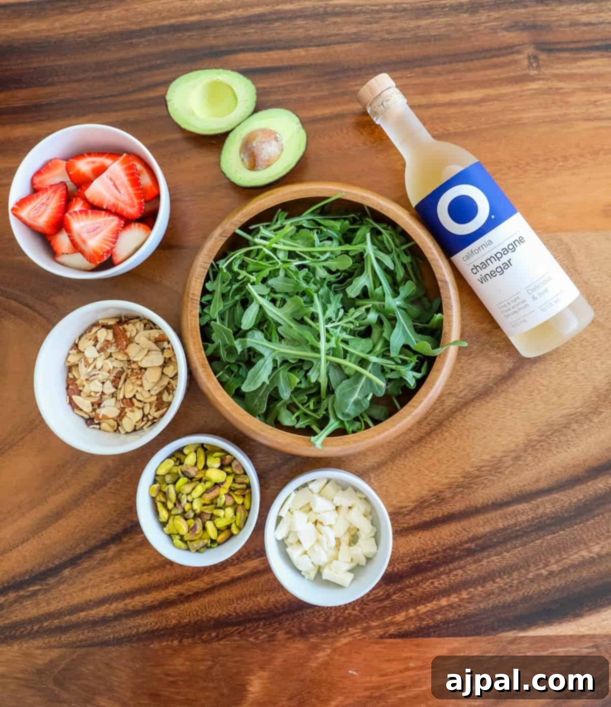 A selection of fresh ingredients including ripe strawberries, mixed nuts, and a bottle of champagne vinegar, ready for preparing a strawberry crunch salad.
