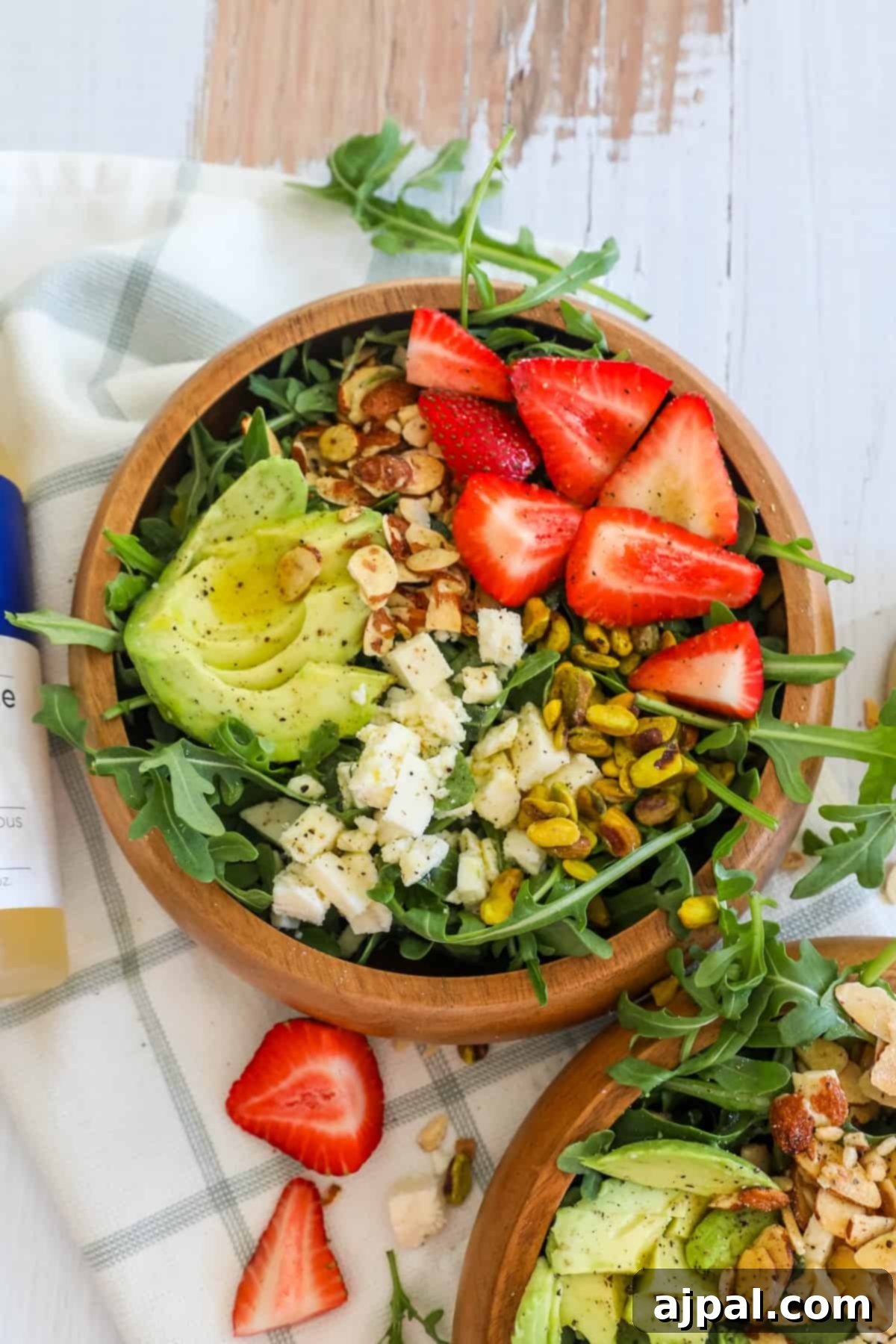 Two vibrant bowls of Strawberry Crunch Salad, featuring sliced avocado, fresh strawberries, and crunchy pistachios, served beautifully.