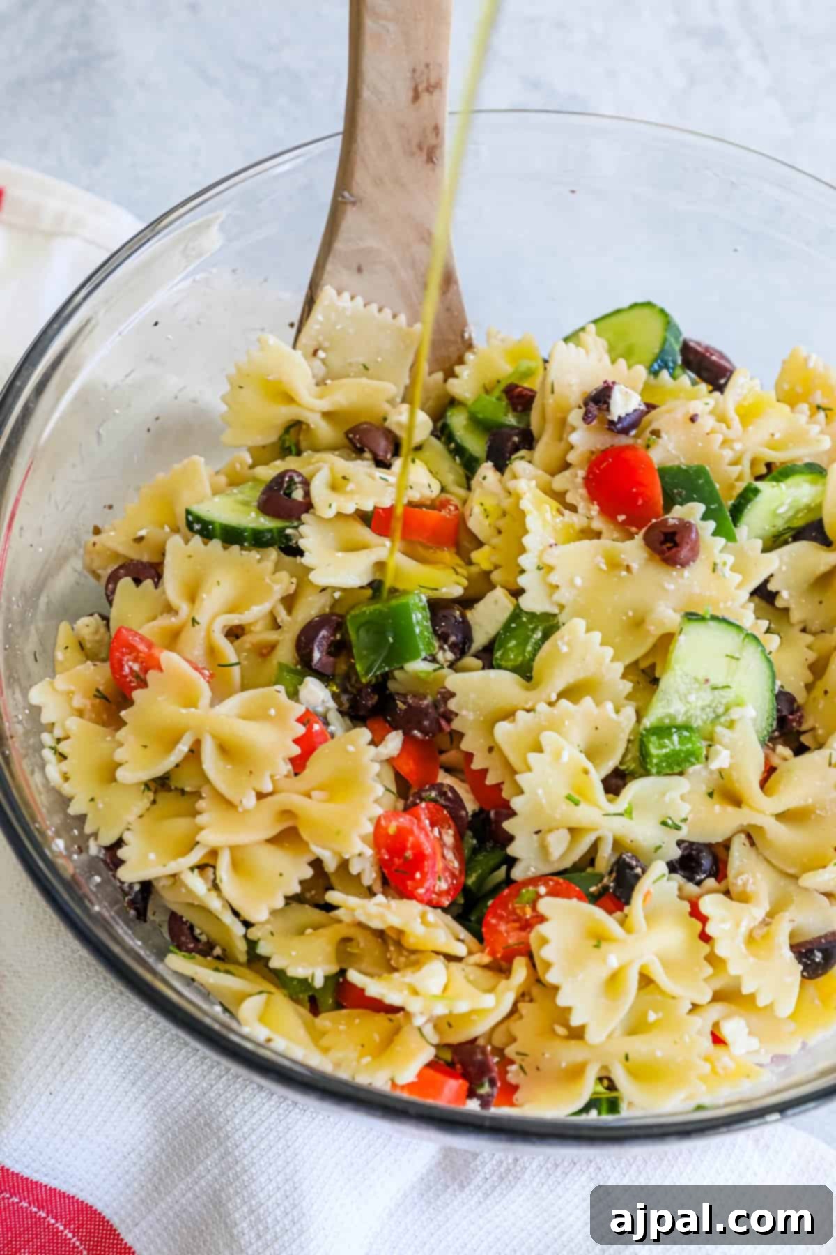 Zesty Greek Pasta Salad 5 Olive oil being drizzled over a bowl of Greek pasta salad.