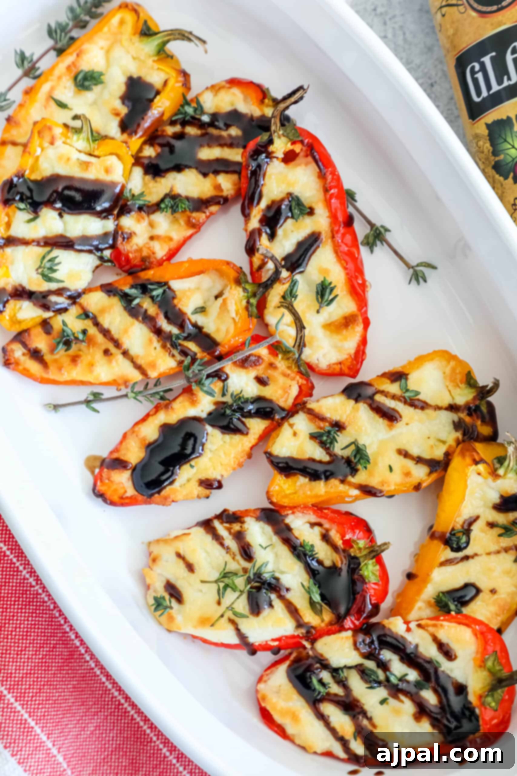 Goat Cheese Stuffed Peppers 12 A pristine white plate holds beautifully grilled mini bell peppers with a side of creamy baked goat cheese. A bottle of high-quality olive oil and a sprig of fresh herbs complete the elegant presentation.