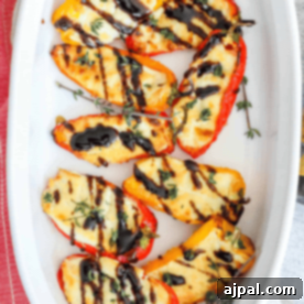 Baked mini bell peppers, perfectly golden and stuffed with creamy goat cheese, nestled in a white dish and garnished with black olives and fresh thyme.
