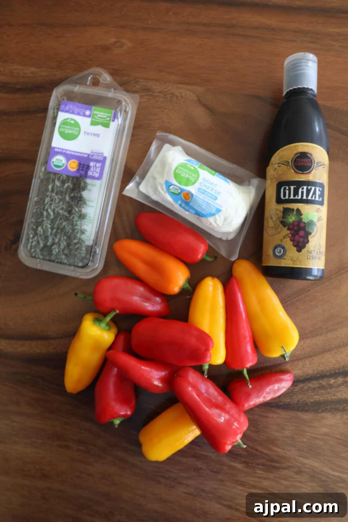 Goat Cheese Stuffed Peppers 5 A selection of fresh ingredients for baked goat cheese peppers displayed on a rustic wooden table, including mini bell peppers, a log of goat cheese, a sprig of fresh thyme, and bottles of balsamic glaze and olive oil, all ready for preparation.